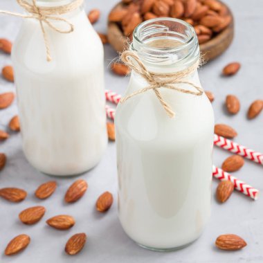 Arkaplanda badem olan cam şişelerdeki badem sütü, kare biçiminde.