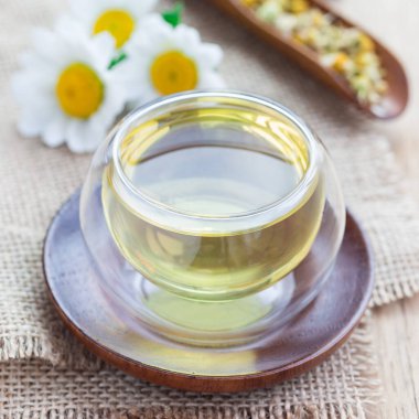 Asya tarzı cam bardakta papatya çayı, papatya çiçeği ve arka planda kuru çay, kare format.