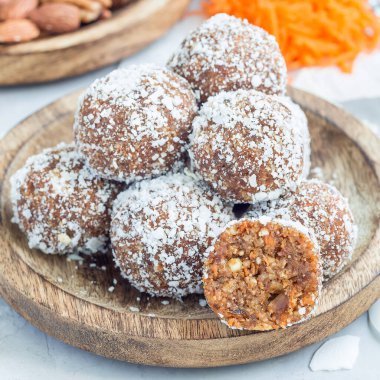 Tahta bir tabakta, havuç, fındık, hurma ve hindistan cevizi taneleriyle ev yapımı sağlıklı paleo enerji topları.