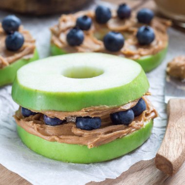 Fıstık ezmesi ve yaban mersinli yeşil elma mermileri ahşap bir masada, kare biçiminde.