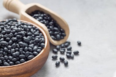 Ahşap bir kasede siyah fasulyeler ve gri beton arka plan kepçesinde, yatay, kopyalama alanı