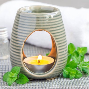 Aroma lambasındaki nane yağı, kaplıca arkaplanlı gri minder, kare biçiminde.