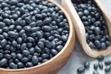 Tahta bir kasede siyah fasulyeler ve gri beton bir arka planda kepçenin içinde, yatay, yakın plan