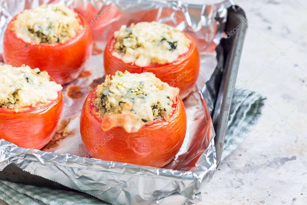 Baked tomatoes stuffed with quinoa and spinach topped with melted cheese in baking dish, horizontal, closeup