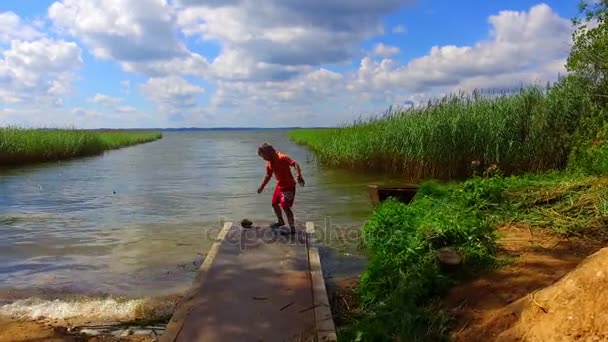 Kluk hraje na břehu jezera zelené trávy — Stock video