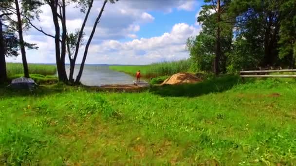 Boy playing on green grass lake shore — Stock Video