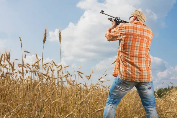 Lovec v čepici a brýle míření zbraní na pole — Stock fotografie