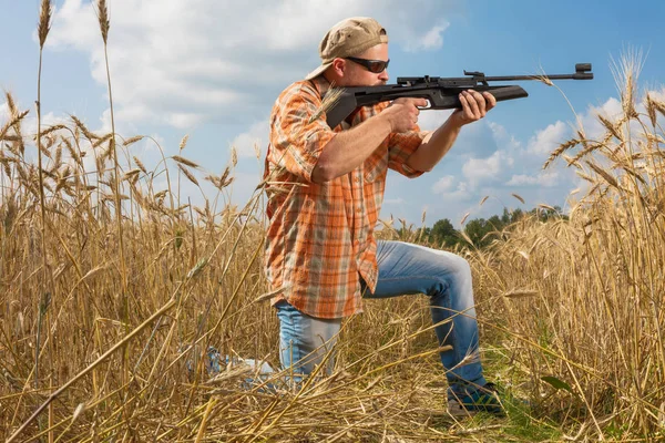 Lovec na čepici a brýle míření zbraní na pole — Stock fotografie