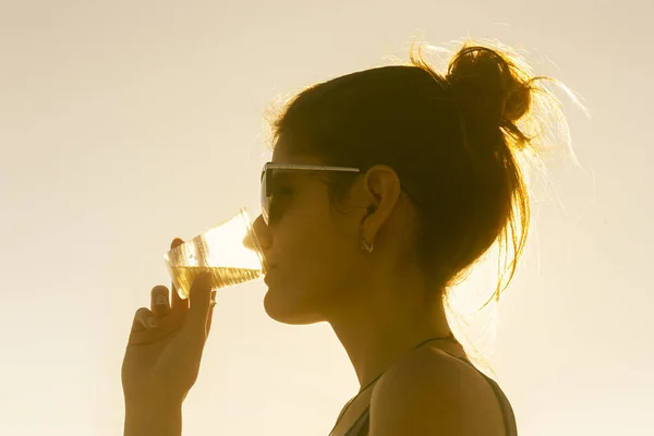 Young attractive woman on the beach at sunset drinking from glass — Stock Photo, Image