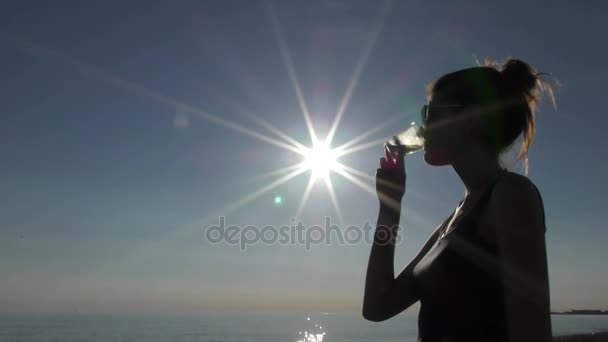 Mladá atraktivní žena na pláži při západu slunce pití ze skla — Stock video
