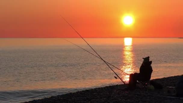 Όμορφη σκηνή με ψαρά σιλουέτα με ράβδο που κάθεται στην παραλία της θάλασσας — Αρχείο Βίντεο
