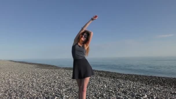 Молодая привлекательная женщина в солнечных очках на галечном пляже — стоковое видео