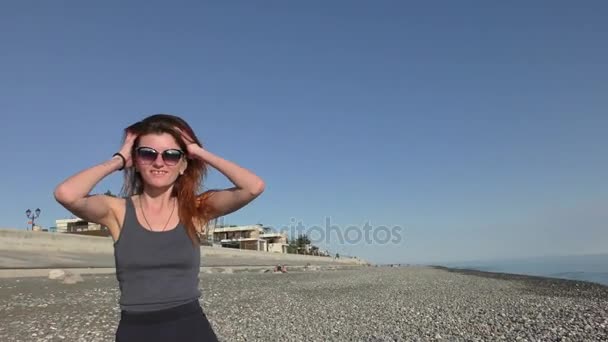 Junge attraktive Frau mit Sonnenbrille am Kiesstrand — Stockvideo