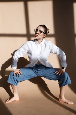 Geniş kot pantolon ve gözlük takan şık bir kadının kapalı mekan portresi. Güzel kız stüdyoda iyi eğlenceler. Moda blogcusu kavramı. Bahar moda konsepti. güzel model
