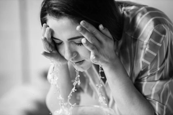 close up of woman washing her face with water. morning procedures in pajama. beauty concept