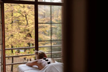 Kaplıca salonundaki sarışın kız masaj yaptırıyor. Spa prosedürü konsepti. Siyah taşlarla sarmaş dolaş bir kız. Uyum kavramı. Kaplıcada rahatlama