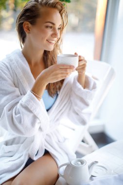 Harika bir cildi ve kafasında beyaz havlusu olan güzel bir kız su içiyor. Kız üstüne spa, sauna, havluyla banyo. Güzellik prosedürü. Sağlık konsepti. Otel servisi konsepti. Kız duştan sonra. Evde dinlen.