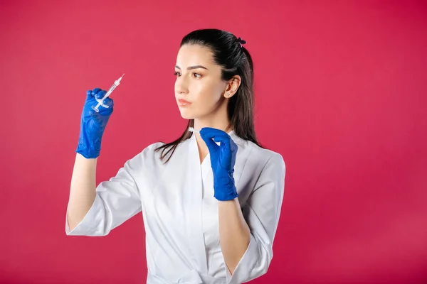 Corona virus nurse. woman doctor in white lab coat with syringe in hands, isolated on red background. Nurse prepares syringe for a shot or vaccination. health care concept. Medical concept. Trial treatment
