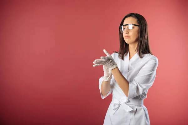 Corona virus Nurse. Medical Student. Nurse Wearing Scrubs and Protective Mask and Goggles. Medical concept. Girl in white clothes put on gloves on red background. Medical stuff protection concept