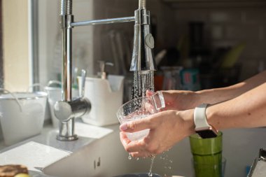 Kadın ellerinin bulaşık şişesi bardağını yıkadığı yeri kapatın. bulaşık konseptini yıka. Modern mutfak. Ekonomik su tüketimi kavramı. Musluktan temiz su dökülüyor. Dünya çapında su krizi sorunu