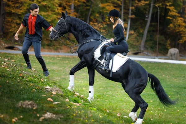 女の子は山の中の湖の近くの秋に公園で馬に乗っている 馬のギャロップに乗った馬男と女 ジョッキーは女に乗るように教える 馬術スポーツの概念 馬に乗る訓練だ — ストック写真