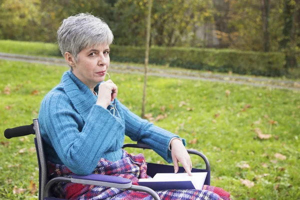 Femme en fauteuil roulant lisant un livre dans le parc — Photo