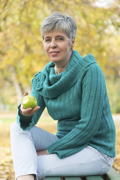 Mulher no parque de outono comendo uma maçã — Fotografia de Stock