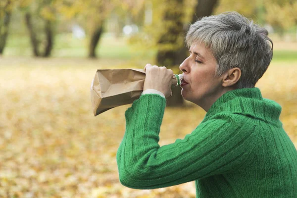 Несчастная женщина в парке пьет алкоголь — стоковое фото