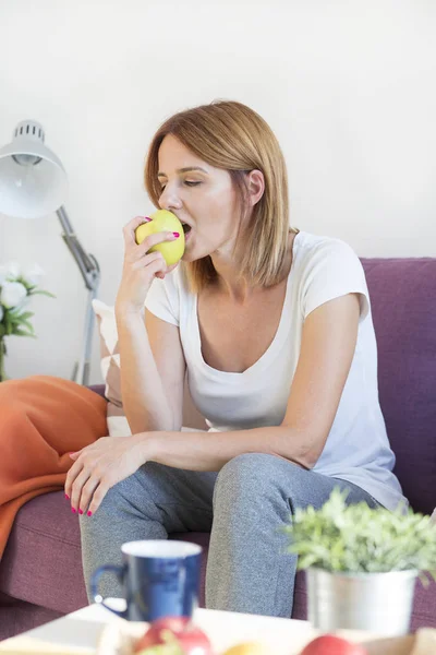 Mulher no sofá na sala de estar comendo uma maçã — Fotografia de Stock