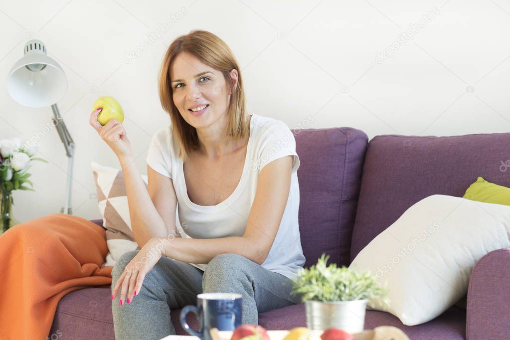  woman on the couch in living room eating an apple