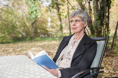 Bir kitap okuma parkta oturan gri saçlı yaşlı kadın