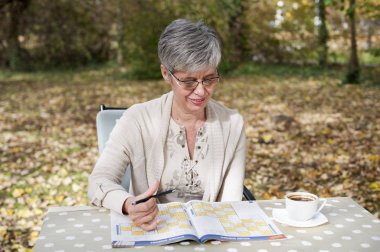 Parkta oturan gri saçlı yaşlı kadın ve sudoku çözer