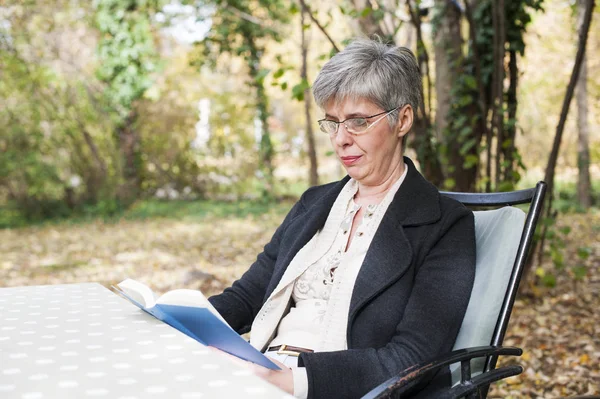 Vanhempi nainen puistossa lukemassa kirjaa — kuvapankkivalokuva