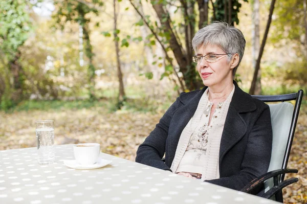 Пенсионерка сидит в парке и пьет кофе — стоковое фото
