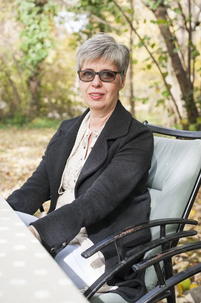 Oudere vrouw met grijze haren zitten in het park — Stockfoto