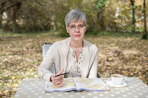 Femeia mai în vârstă în parc și rezolvă sudoku — Fotografie, imagine de stoc