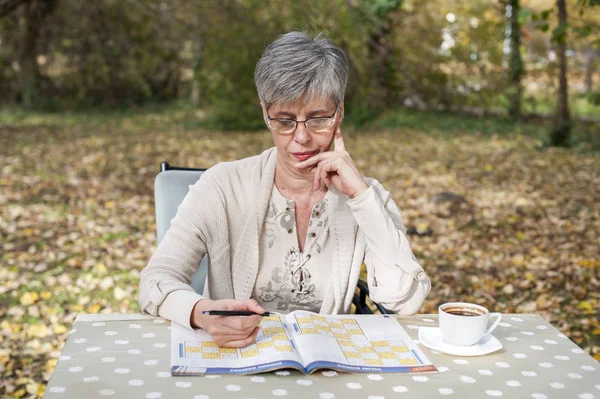 Idős asszony a parkban, és megoldja a sudoku — Stock Fotó