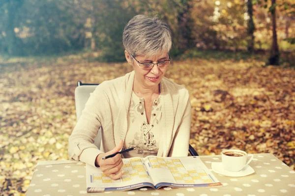 Starsza kobieta w parku i rozwiązuje sudoku — Zdjęcie stockowe