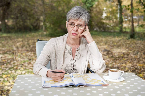 Oudere vrouw in het park en lost sudoku — Stockfoto