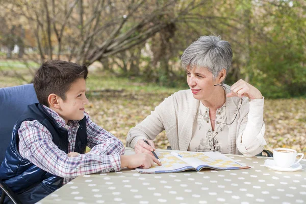 Older woman with grandson in the park and solves sudoku — Stock Photo, Image