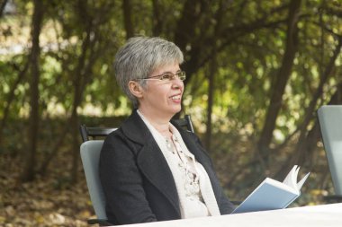 Parkta kitap okuyan yaşlı bir kadın.