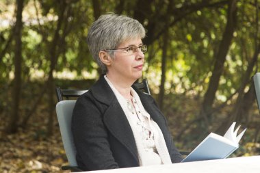 Parkta kitap okuyan yaşlı bir kadın.