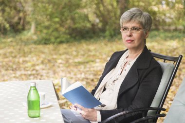 Parkta kitap okuyan yaşlı bir kadın.