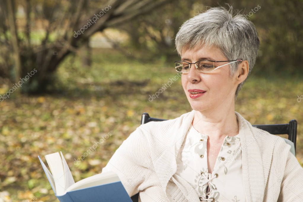 Older woman in the park reading a book