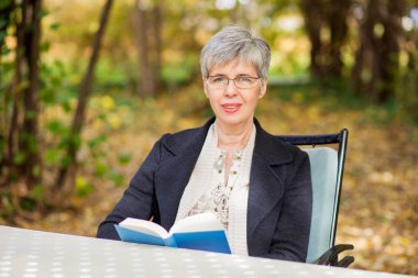 Parkta kitap okuyan yaşlı bir kadın. 