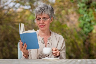 Parkta kitap okuyan yaşlı bir kadın. 