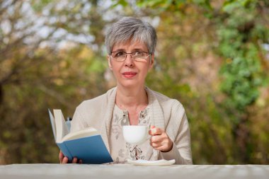 Parkta kitap okuyan yaşlı bir kadın. 