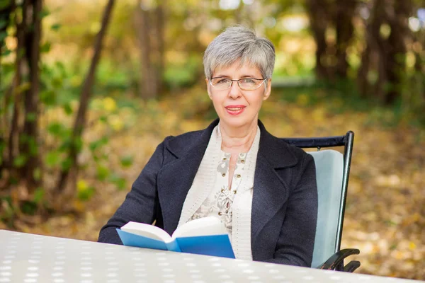 Oudere vrouw in het park het lezen van een boek — Stockfoto