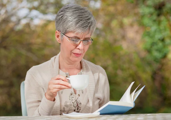 O femeie mai în vârstă în parc citind o carte — Fotografie, imagine de stoc