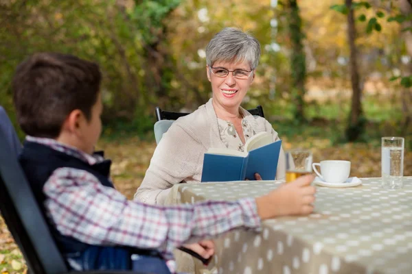 Mujer mayor con nieto leyendo un libro, tomando café y hablando — Foto de Stock